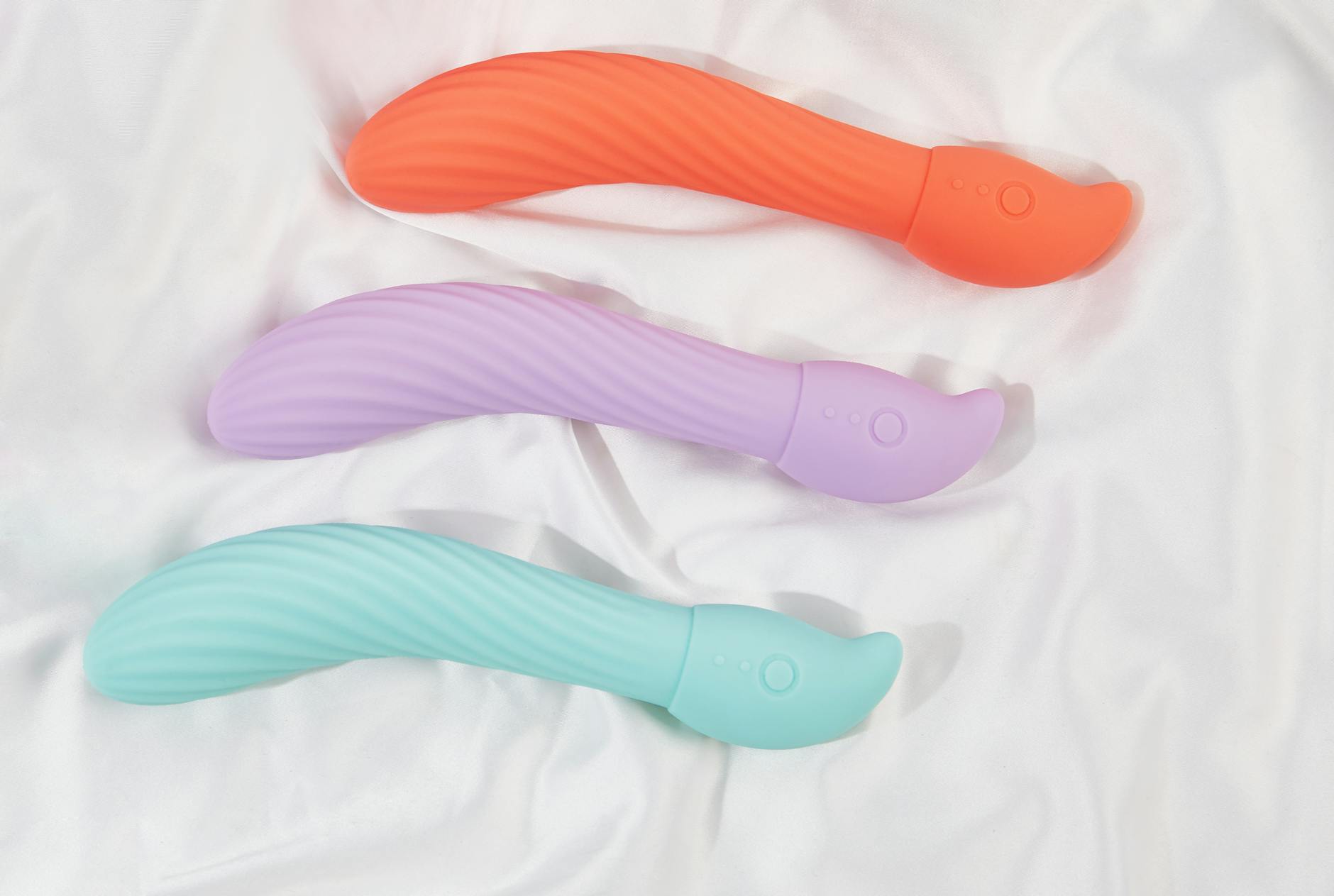 Three colorful clitoral vibrators arranged on white fabric, highlighting their smooth texture and design