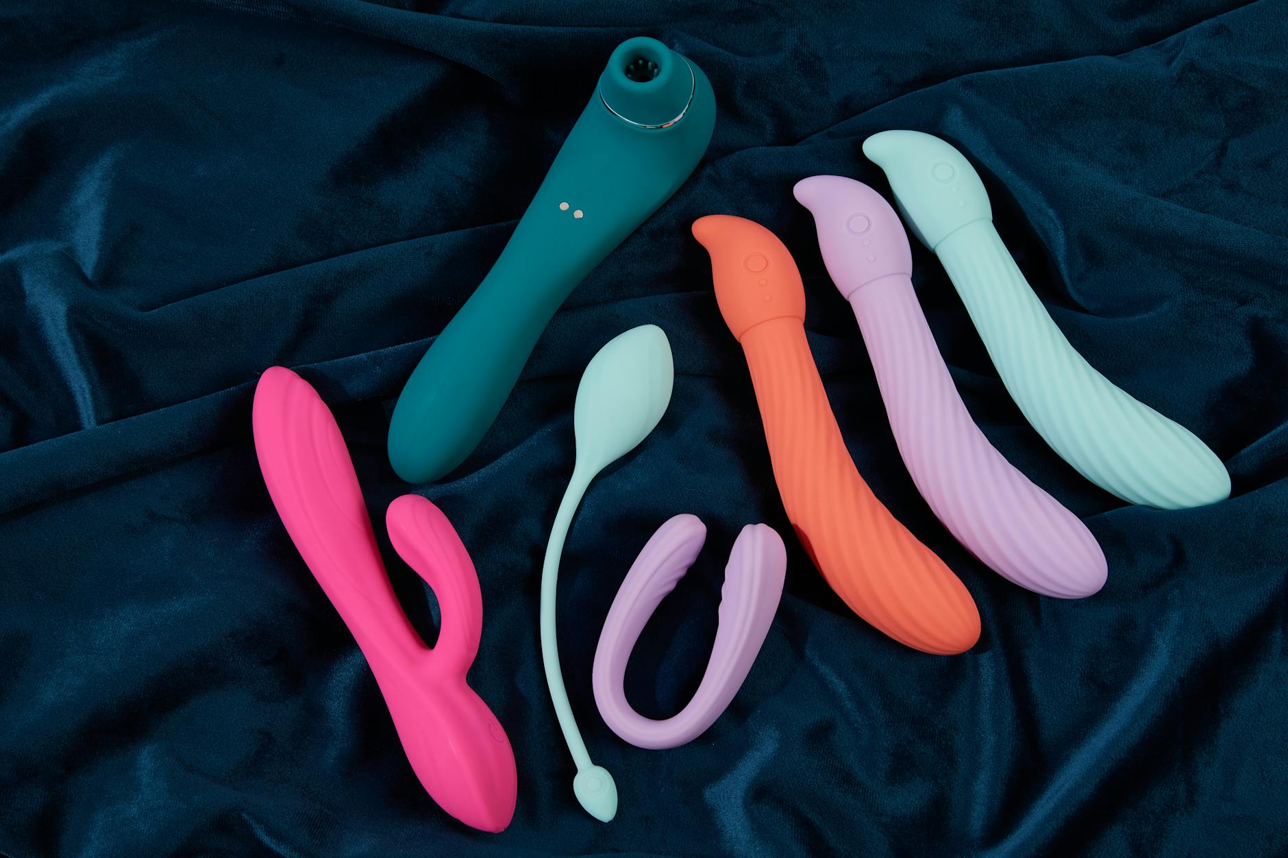Vibrant display of silicone sex toys on dark blue fabric, showcasing various colors and shapes.