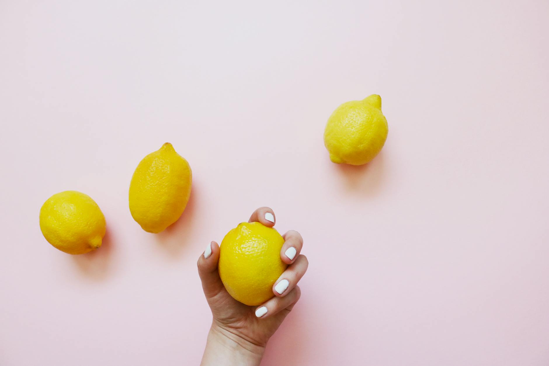 A hand holding a lemon on a soft pink background, symbolizing renewed sensitivity and pleasure.
