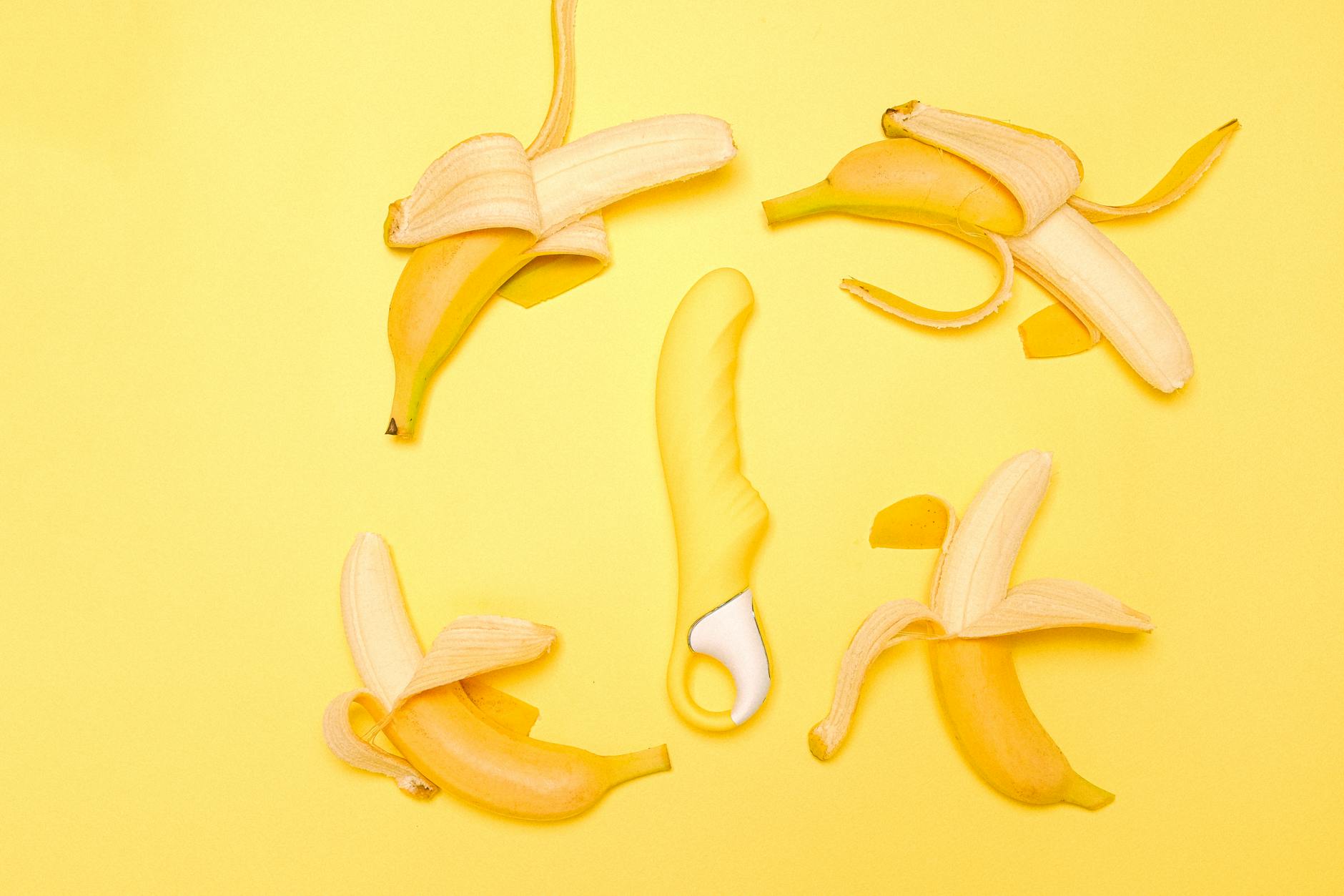 Yellow silicone lemon vibrator surrounded by fresh lemons on a bright yellow surface