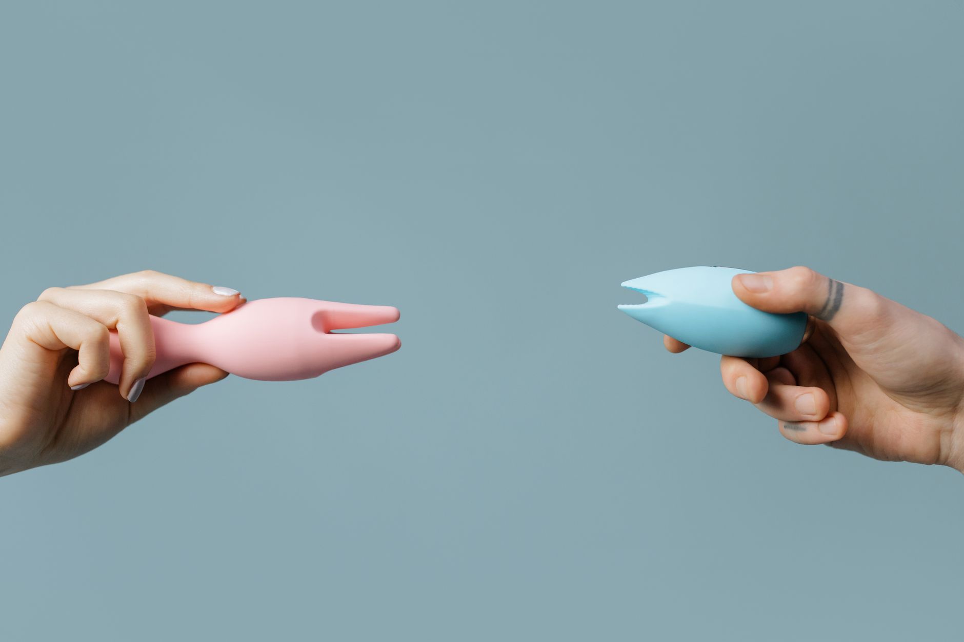 Hand reaching across a table of different colorful vibrators to explore options
