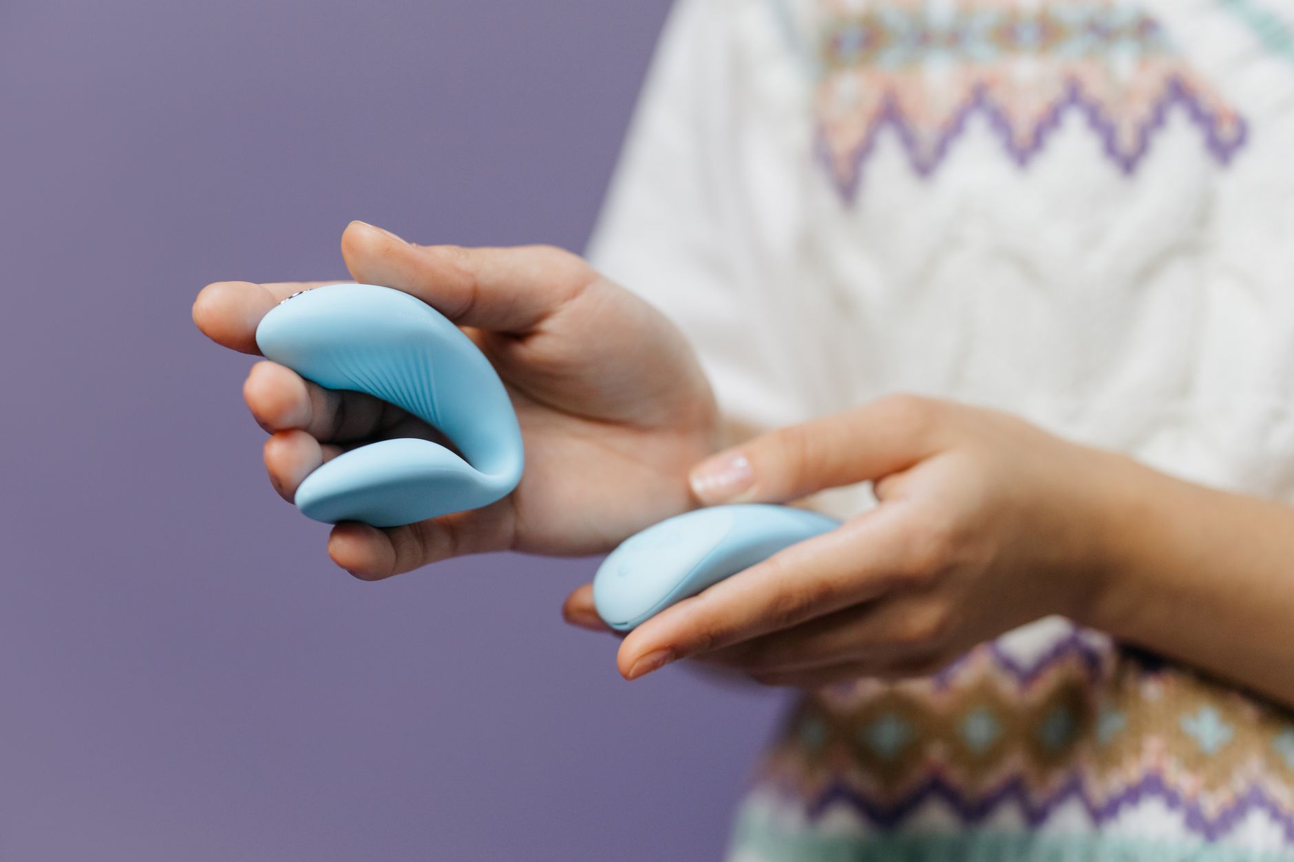 Mãos segurando um vibrador de sucção azul brilhante contra fundo roxo, promovendo bem-estar sexual