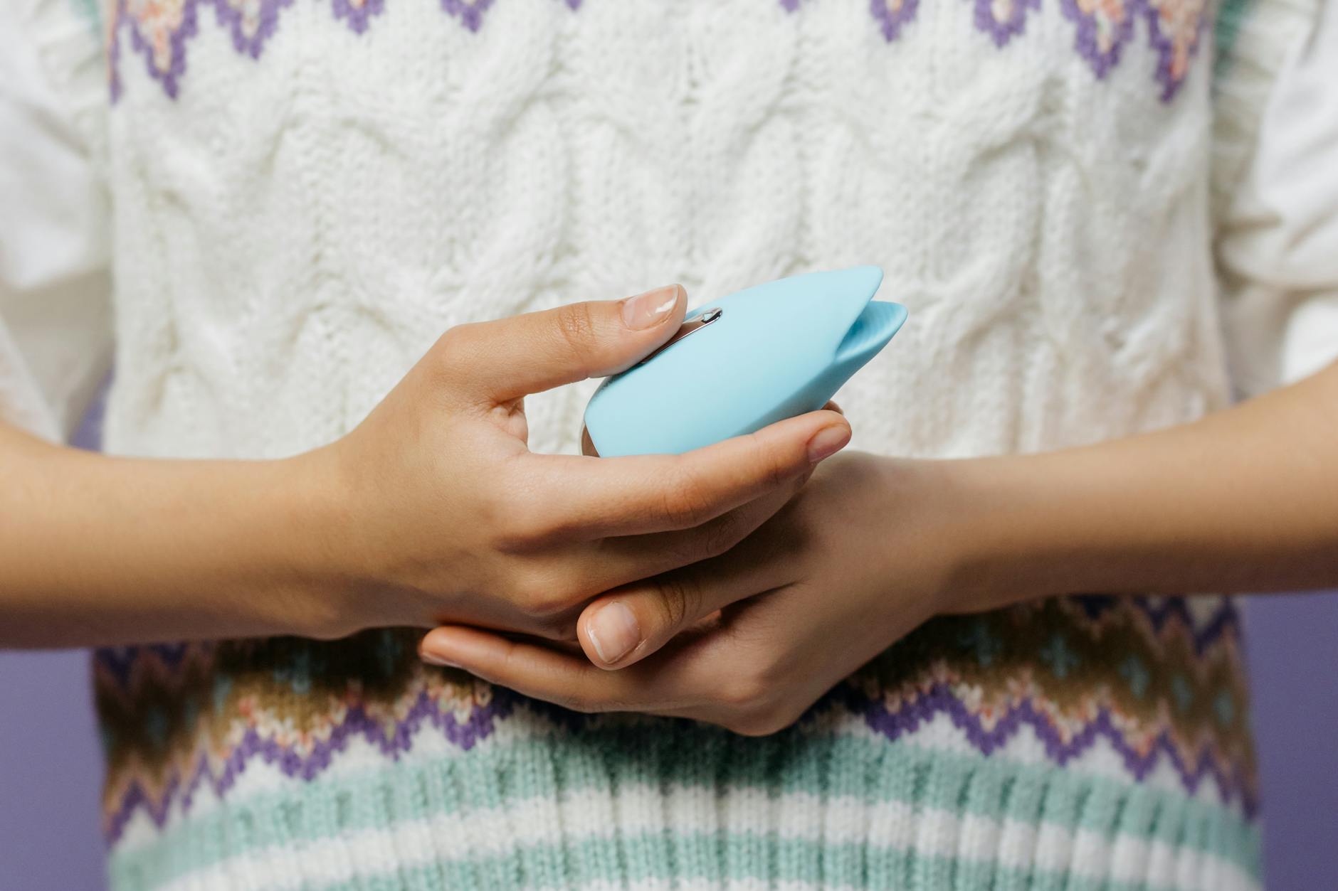 Close-up of hands holding a blue lemon vibrator against a cozy knitted sweater.