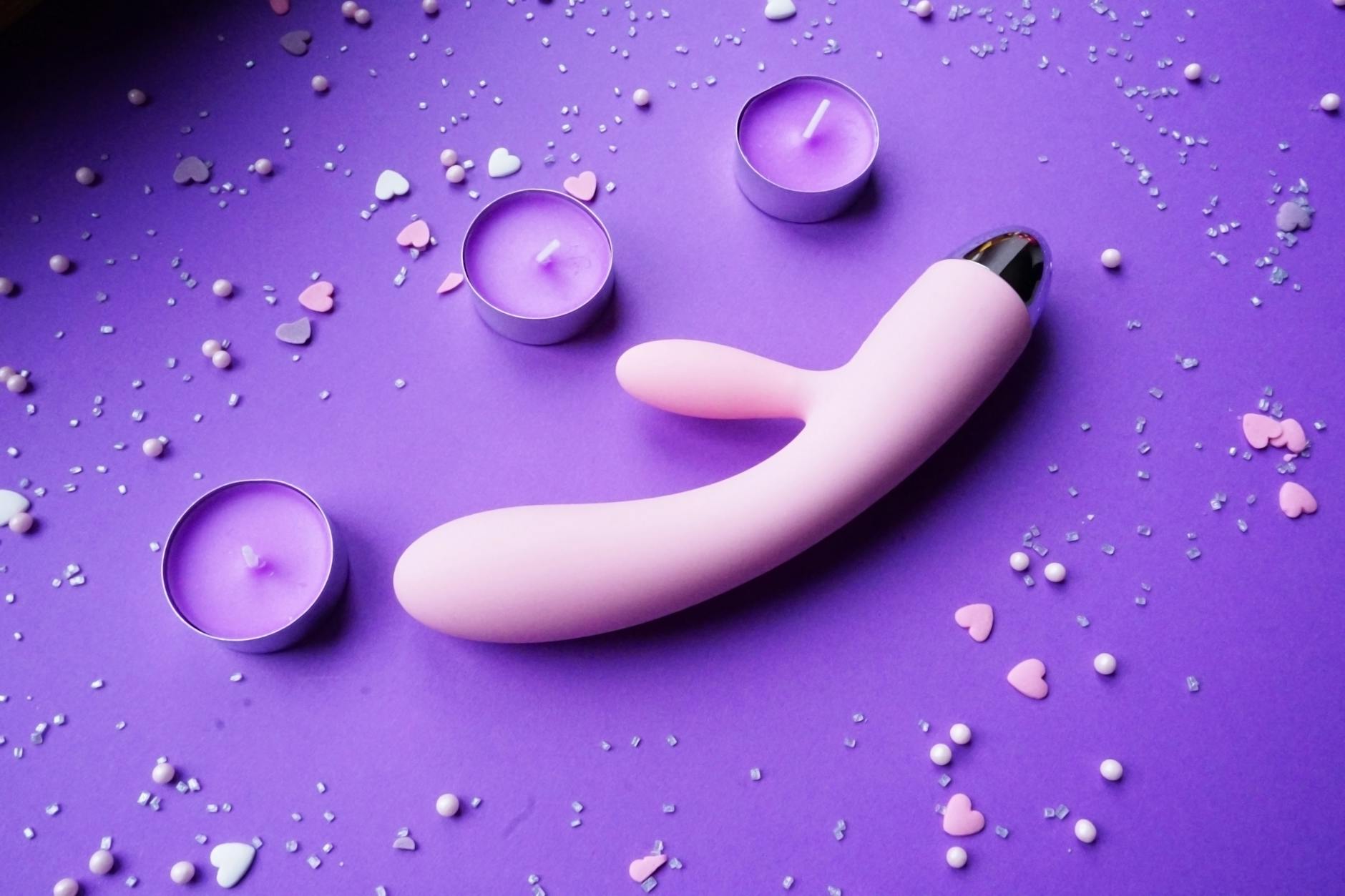 Pink lemon vibrator on purple background with heart confetti and candles